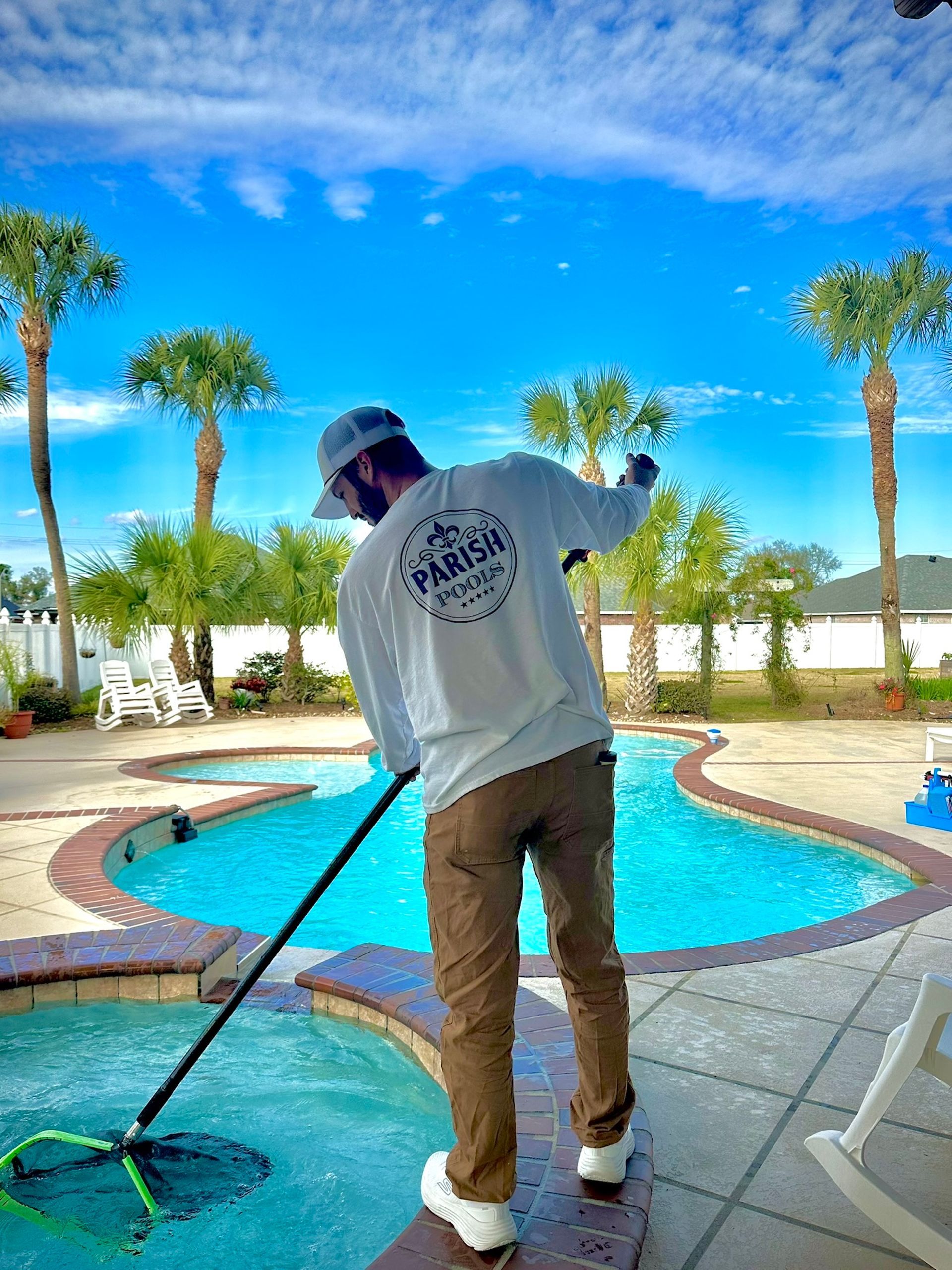 Person in white shirt and khaki pants cleaning a pool with the 