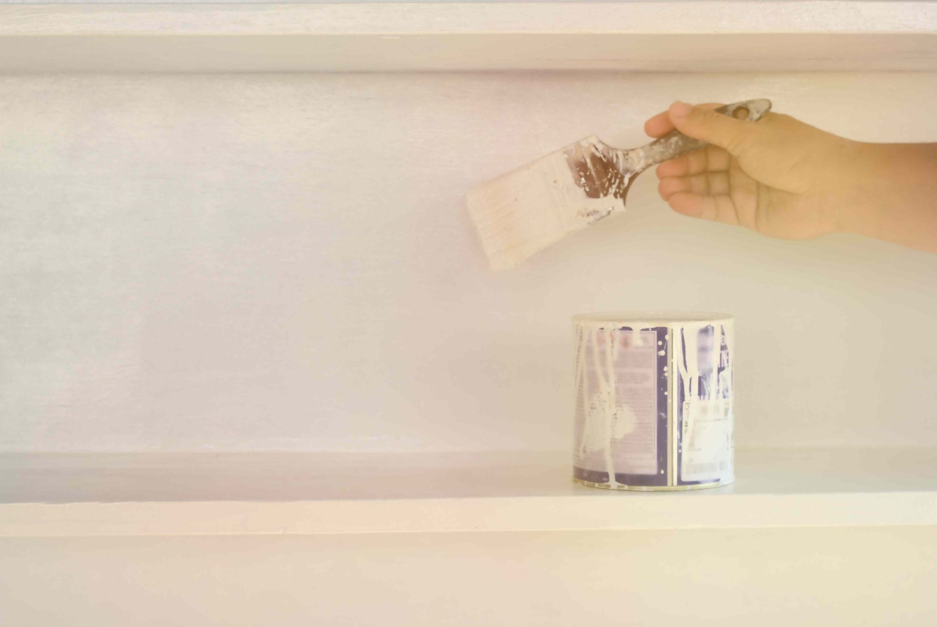 A person is painting a wall with a brush next to a can of paint.