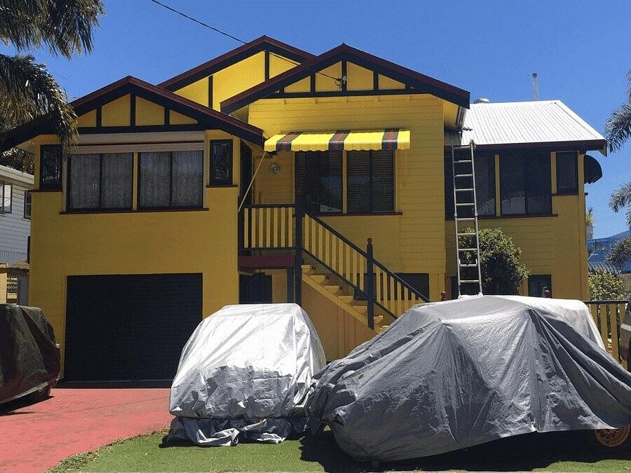 A Yellow House With Two Cars Parked In Front Of It — Pete's Painting Solutions In Kewarra Beach, QLD