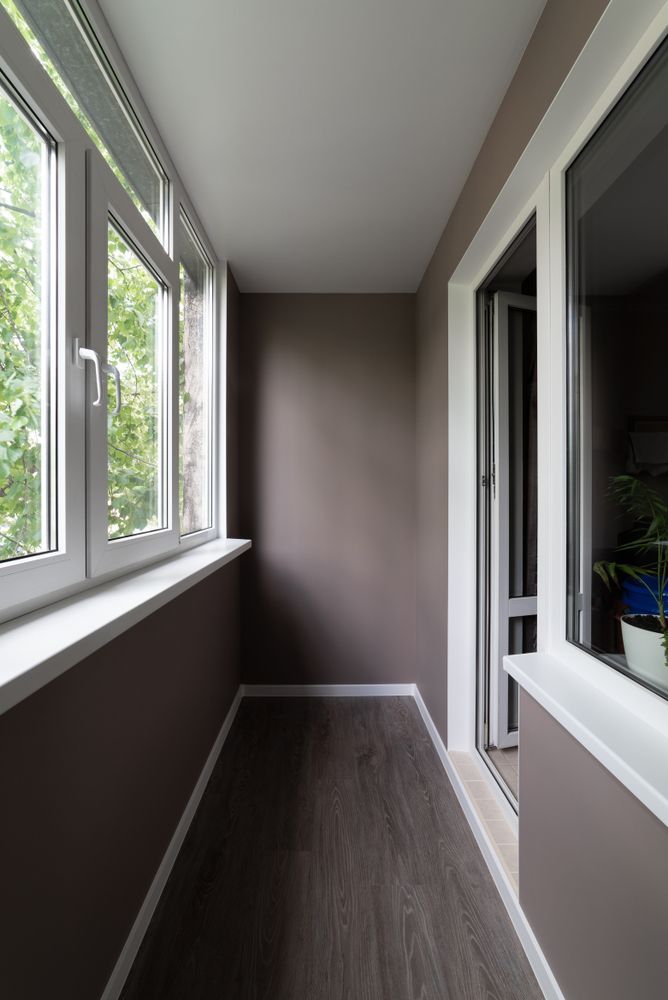 Narrow, Brown-walled Balcony With Dark Wood-look Flooring, White Trim, and a Window