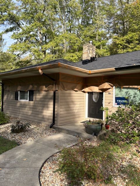 Beige house with black roof, chimney, and door; curved walkway and shrubbery.