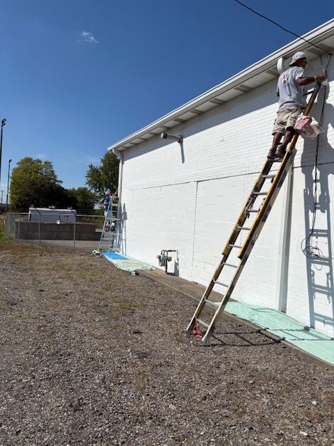 Person on a ladder painting the white exterior of a building on a sunny day.