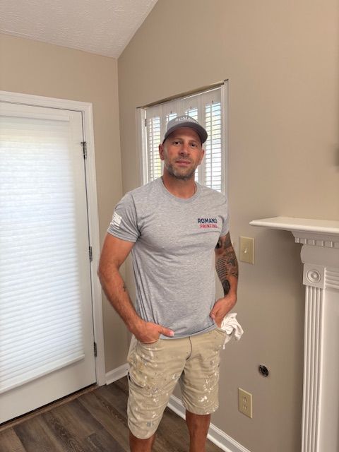 Man in gray shirt and tan shorts standing in a room, hands in pockets.