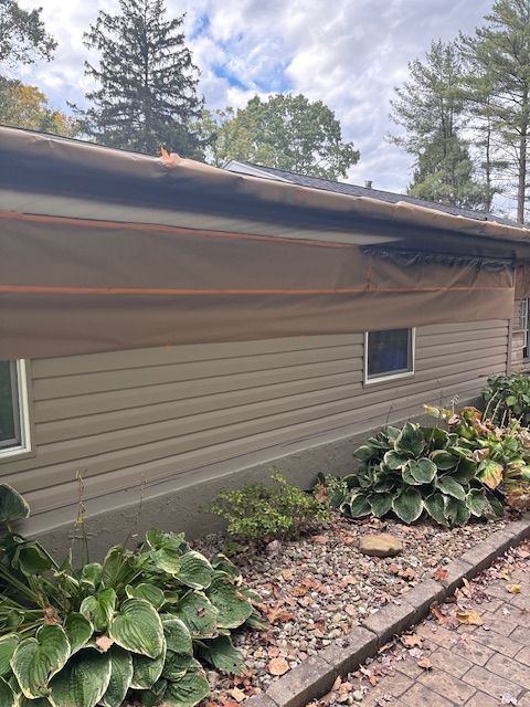 Tan house exterior with brown tarp covering the roof and siding. Hostas and a stone path in front.