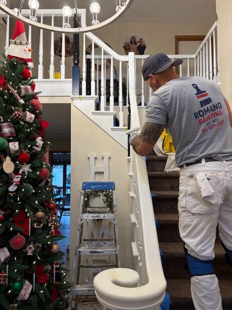 Painter in white pants and a grey shirt painting a staircase. Christmas tree in the background.