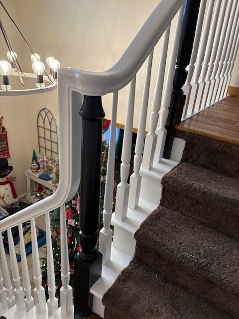 Staircase with brown carpet steps, white spindles, and black posts supporting a white handrail.