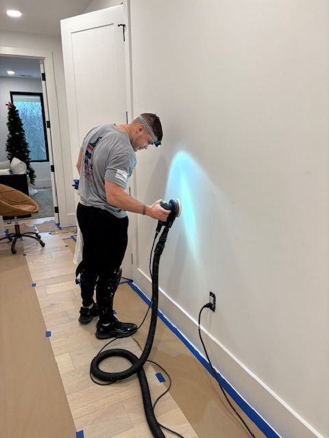 A person sanding a white wall with a sander, wearing a headlamp.