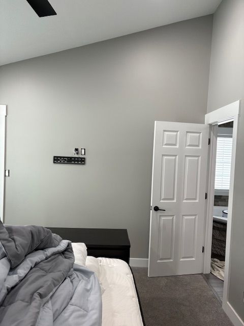 Bedroom with gray walls, white door to bathroom, black bench, and a bed with gray comforter.