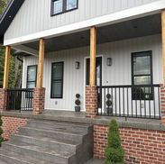 Gray house with a porch. Brick and wooden columns, black railings, and gray steps.