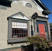Tan building with red door, bay window, and hanging sign.