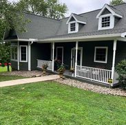 Dark green house with white trim, porch, and two dormer windows under a gray roof.
