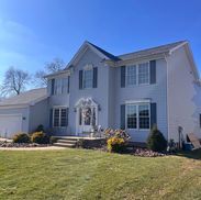 Two-story light blue house with dark blue shutters, on a green lawn, under a blue sky.