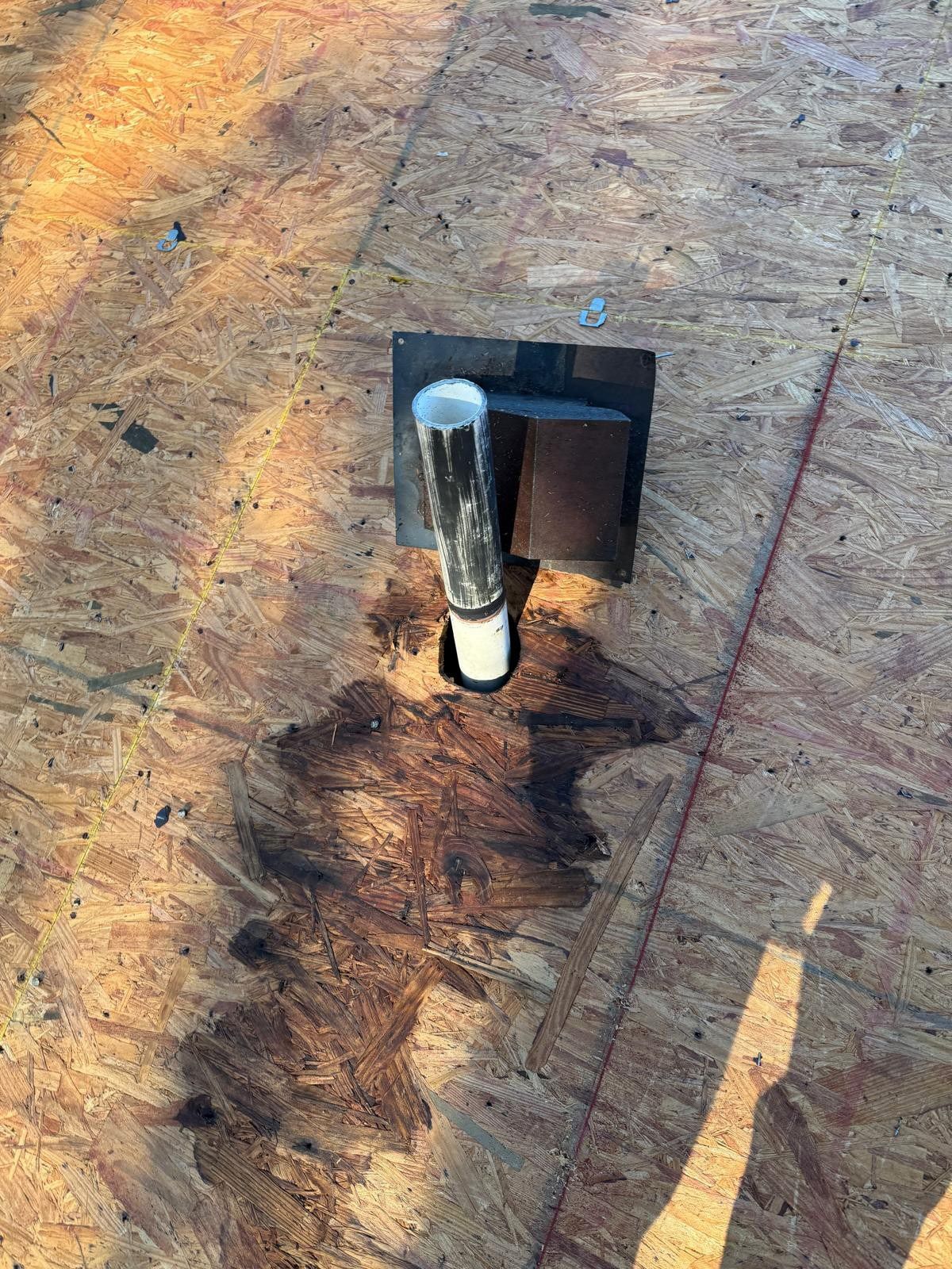 Roof vent pipe on a wood surface, surrounded by dark staining.