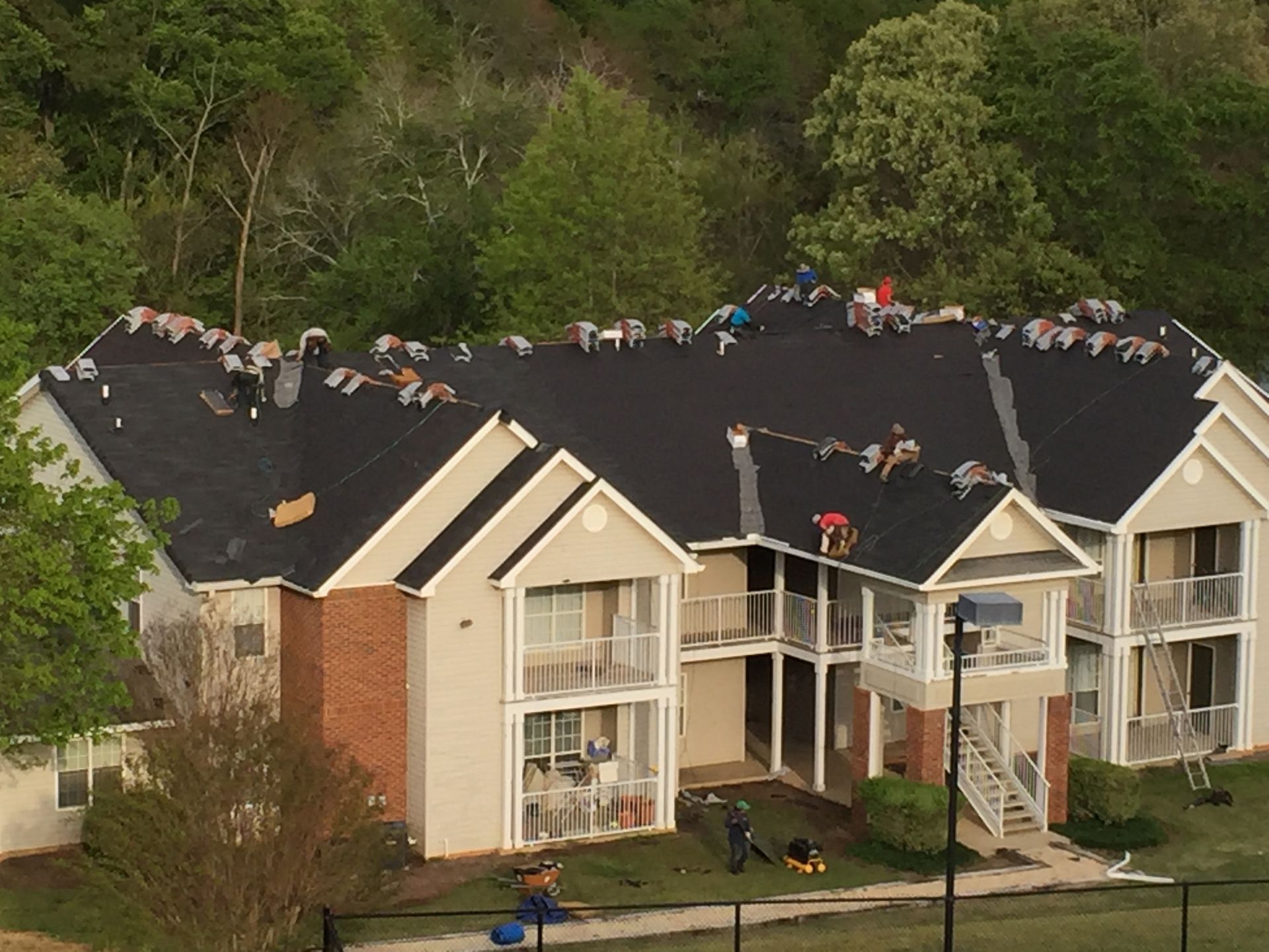 Roofers working on a residential building with a black shingle roof.