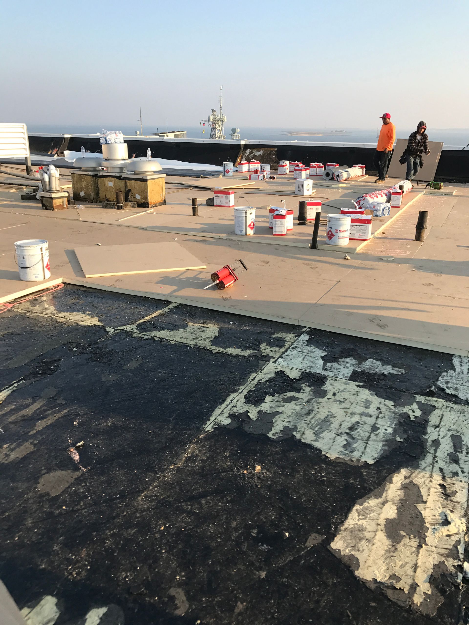 Roof repair: Workers on a rooftop with paint buckets and tools, partially completed project.