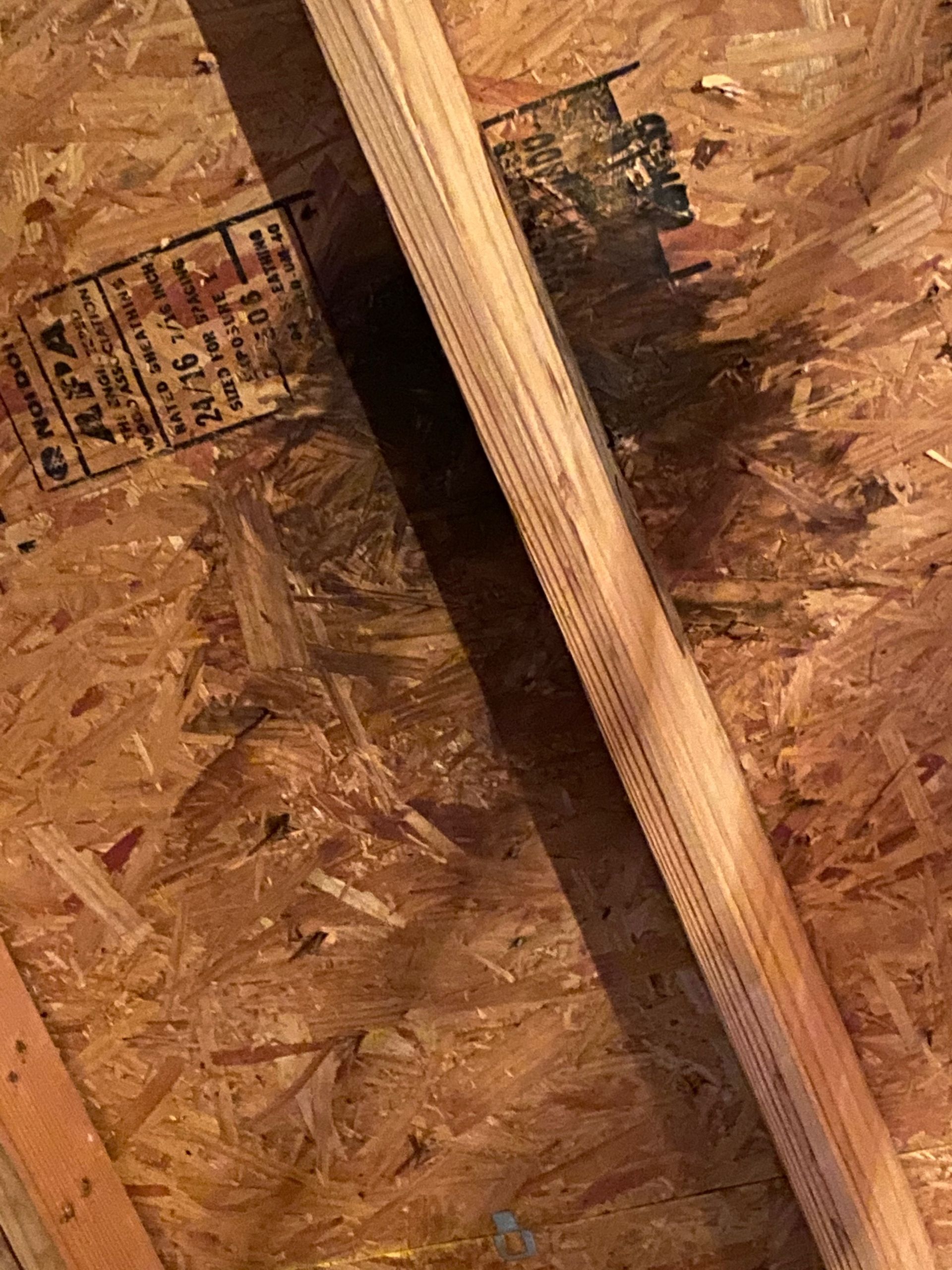 Close-up view of an unfinished attic space with a wooden beam and oriented strand board (OSB) material.