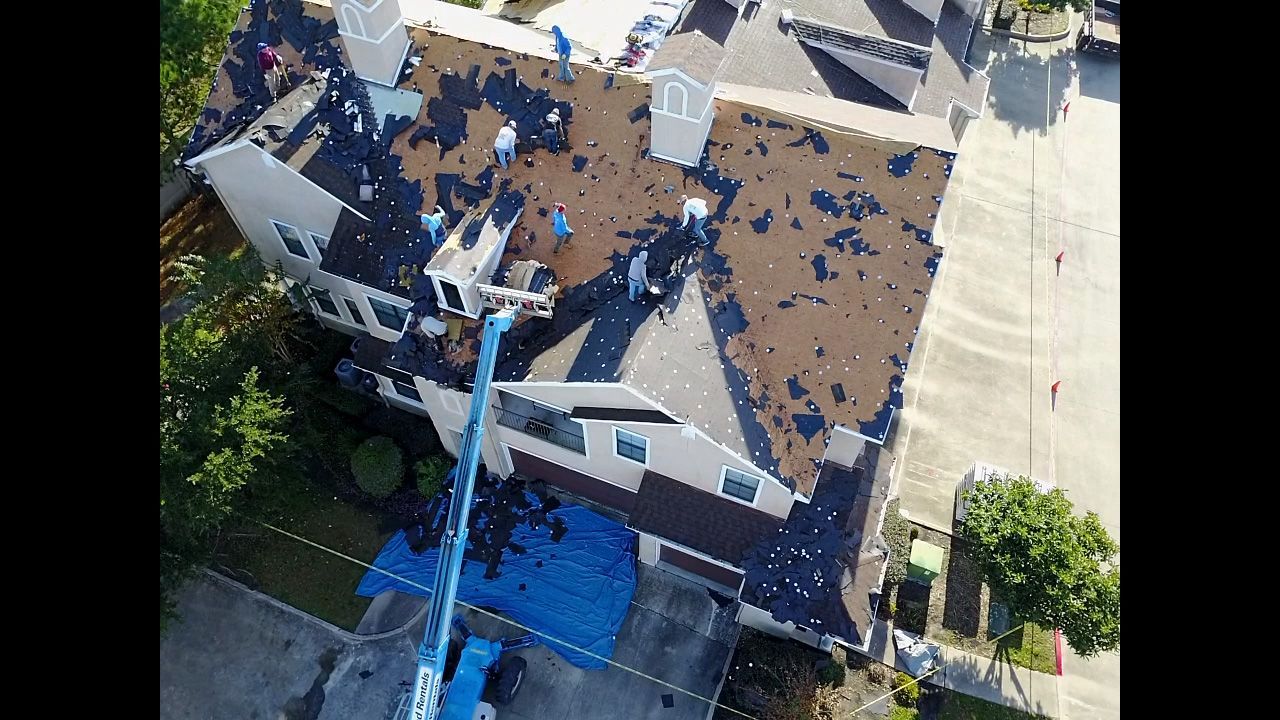 Roof being repaired on a multi-story building; debris, a blue lift, workers.