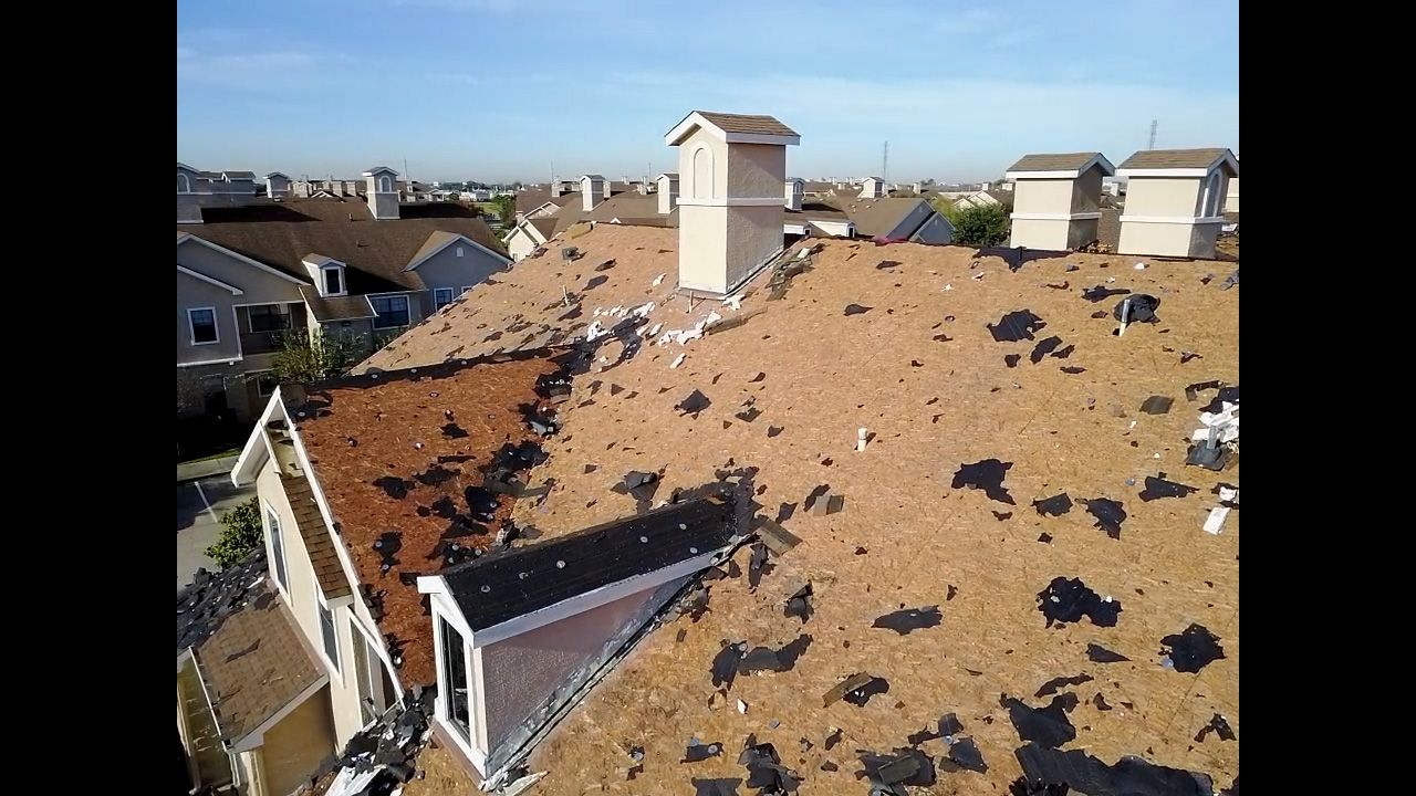 Damaged roof with missing shingles; chimneys and rooftops in background.