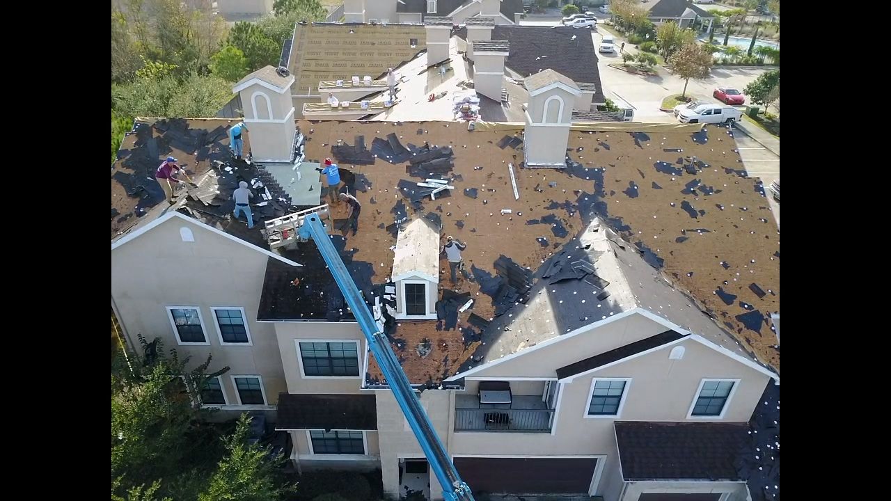 Roofers working on a residential building's rooftop, using a lift. Scattered debris is visible.