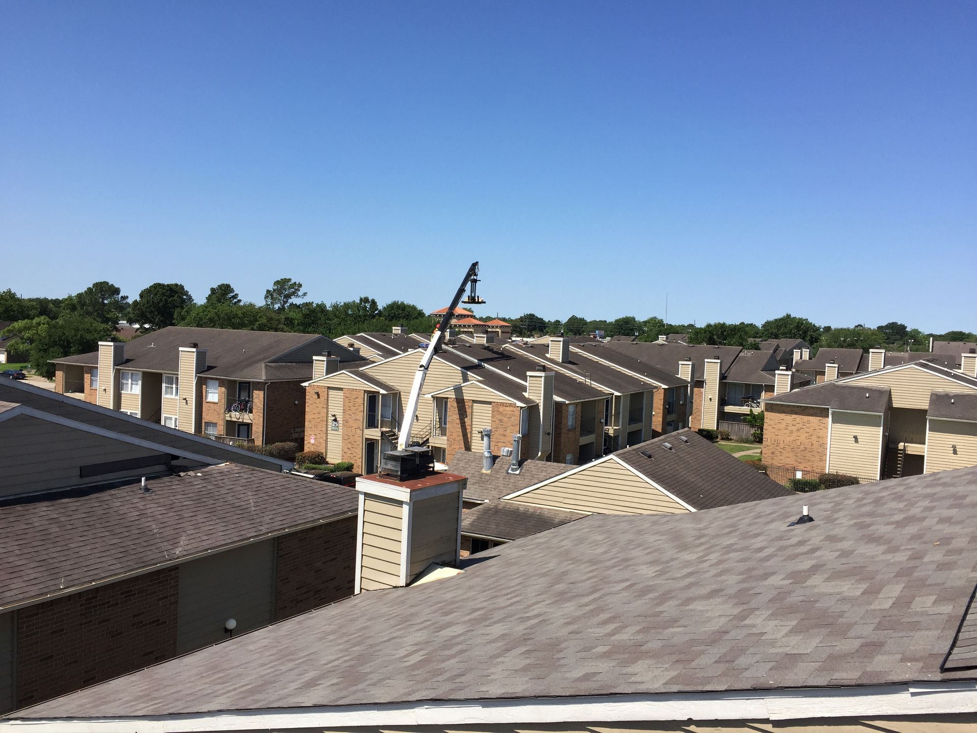 Rooftop view of apartment buildings with an aerial lift being used. Clear, sunny sky.
