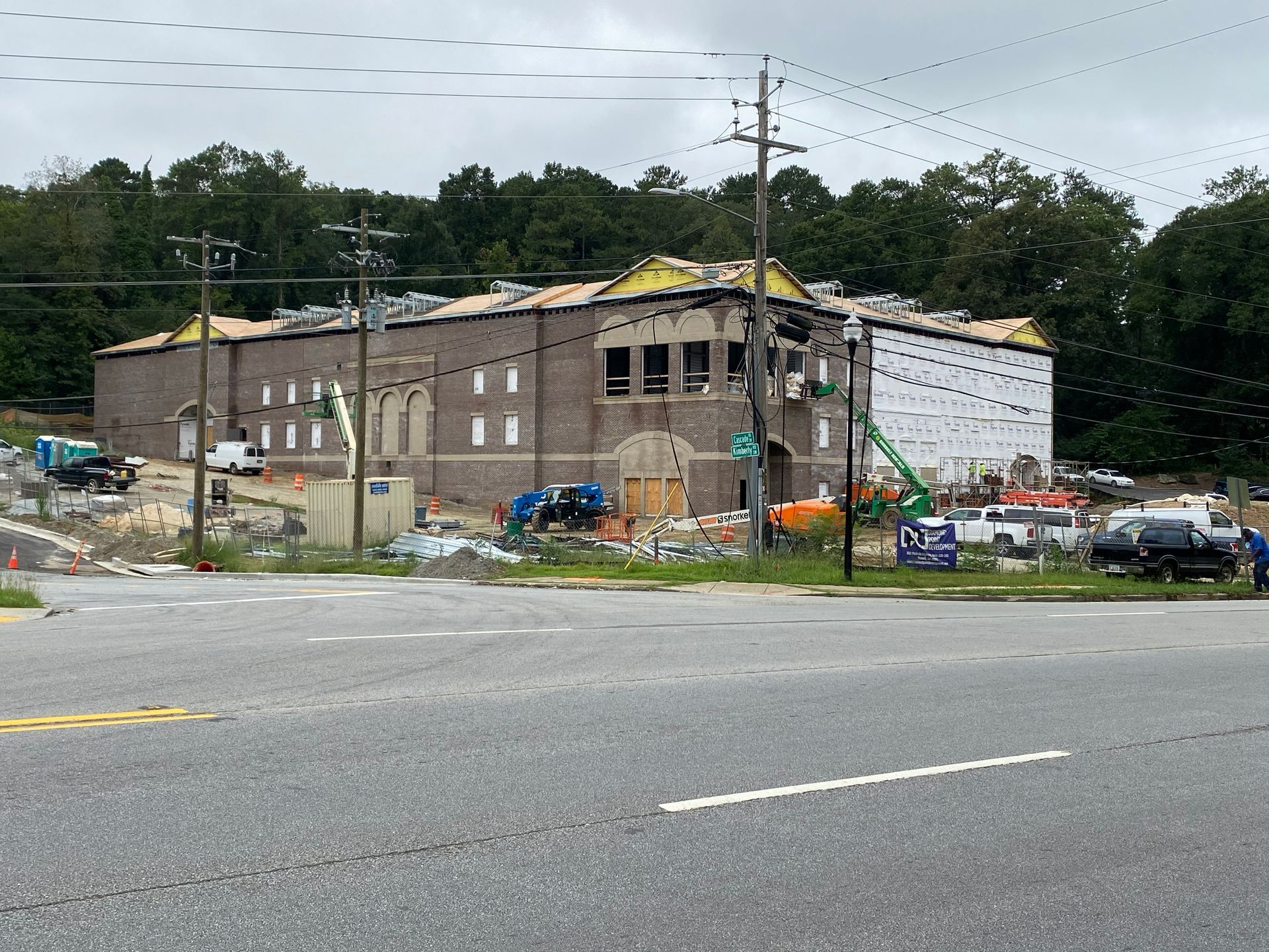 Building under construction with scaffolding, surrounded by equipment and trees.