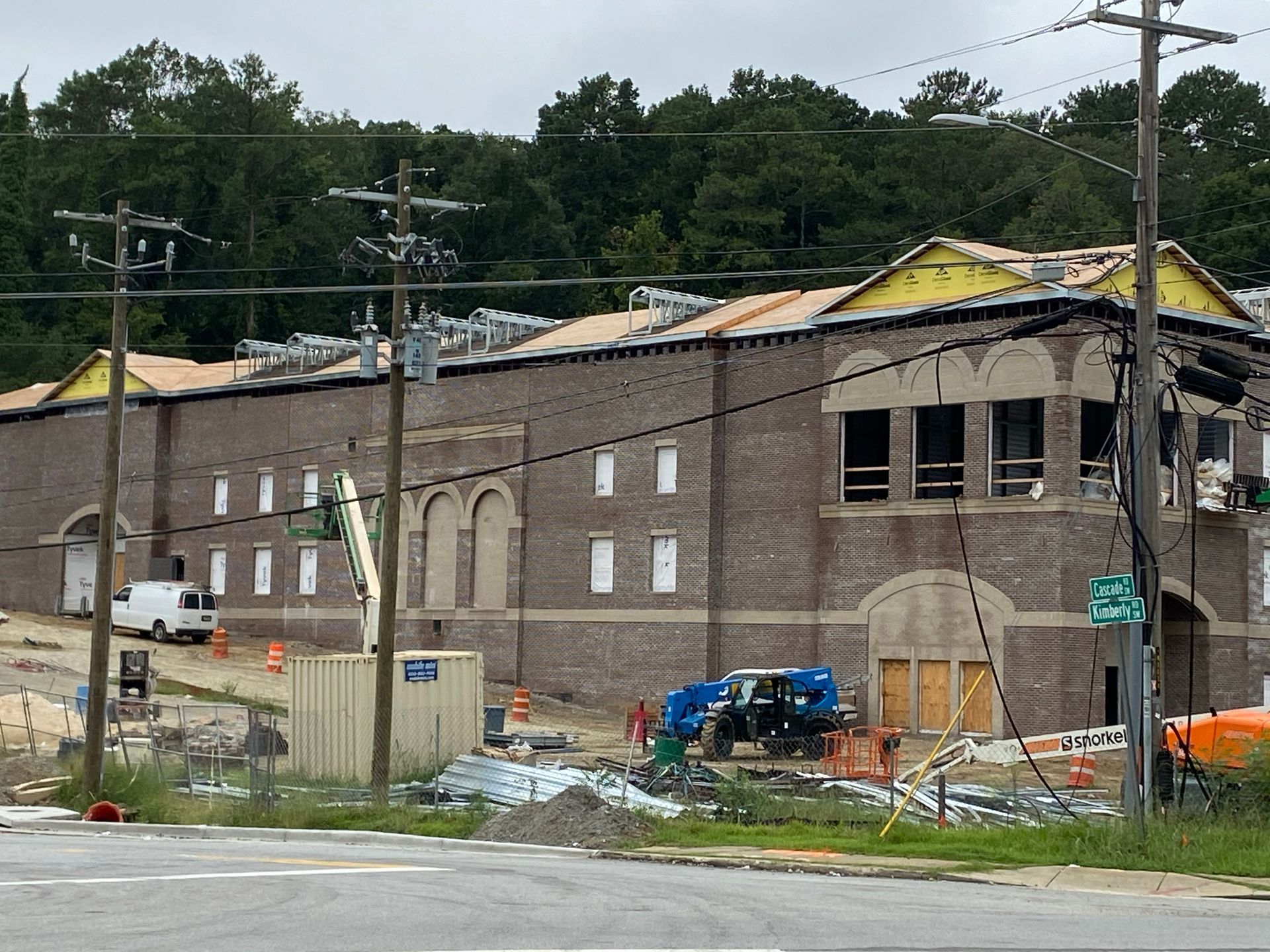 Construction site; brick building with missing roof section, equipment, and utility poles in front.