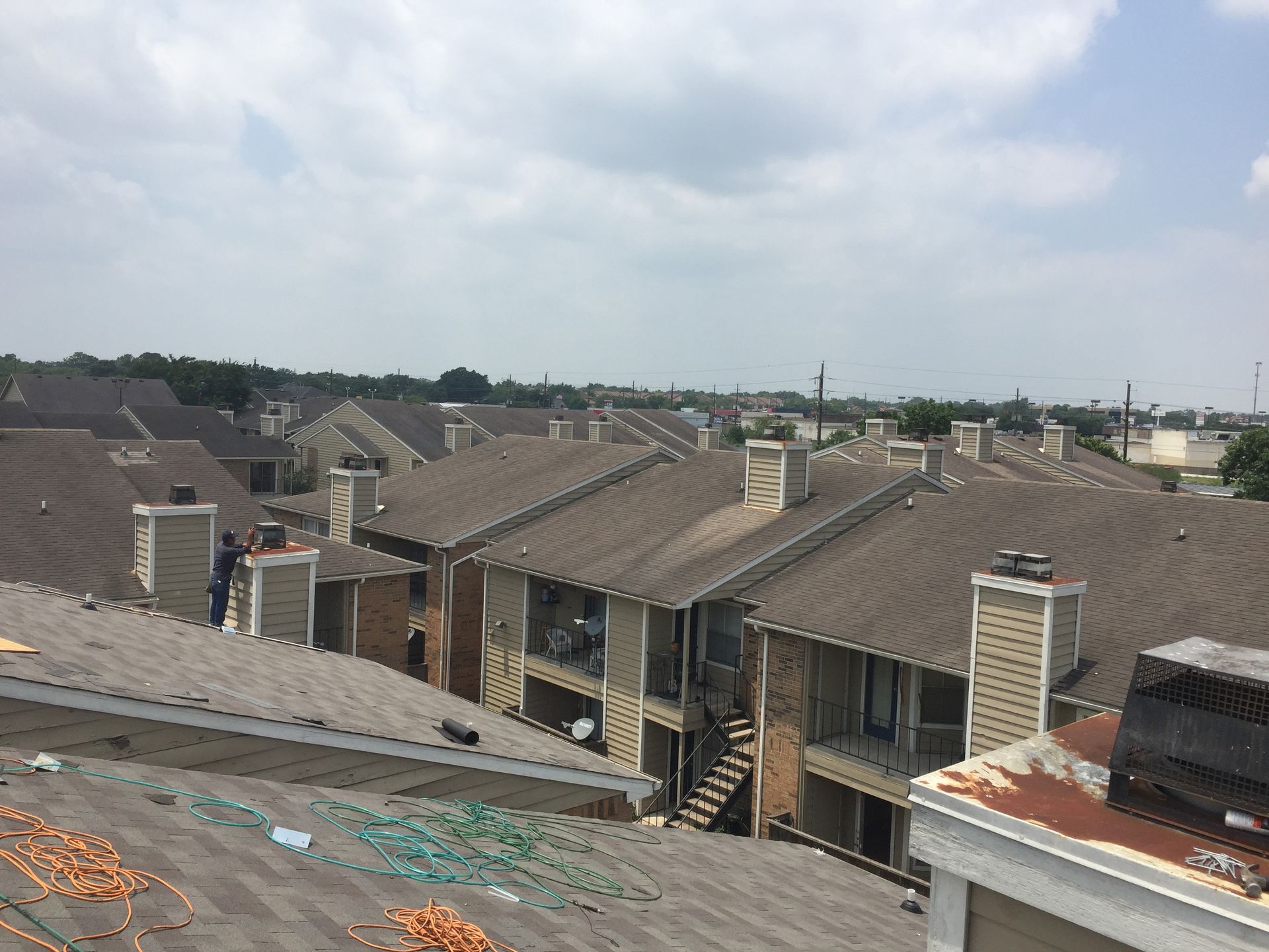 Overhead view of multiple apartment buildings with brown roofs under a cloudy sky.
