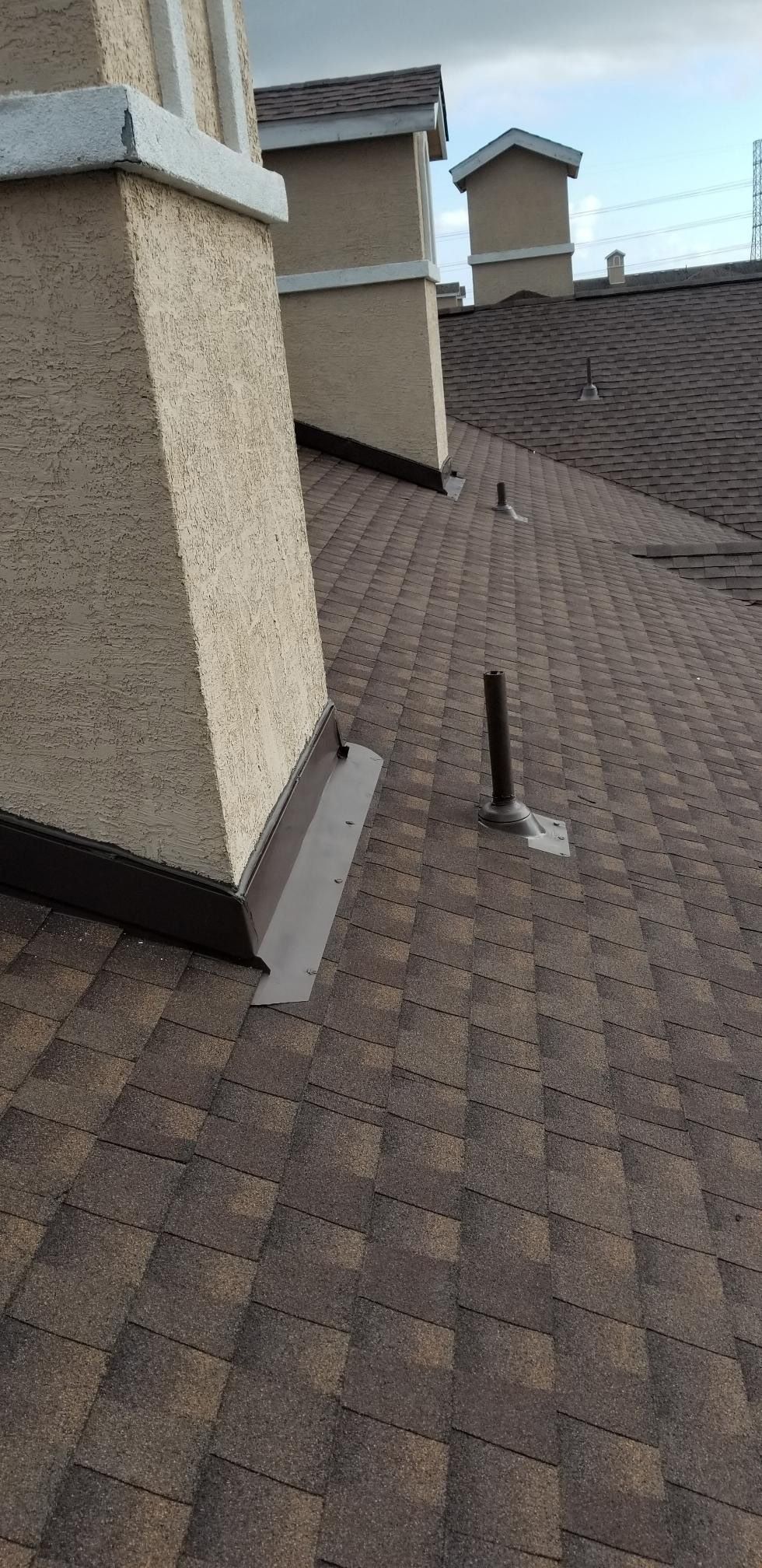 A roof with brown shingles, chimneys, and a pipe. The sky is visible.