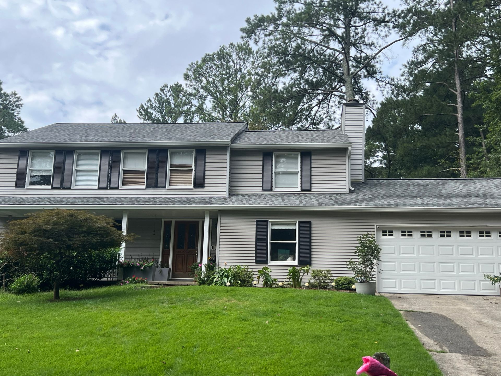 Two-story house with gray siding, black shutters, white garage door, and green lawn. Overcast sky.