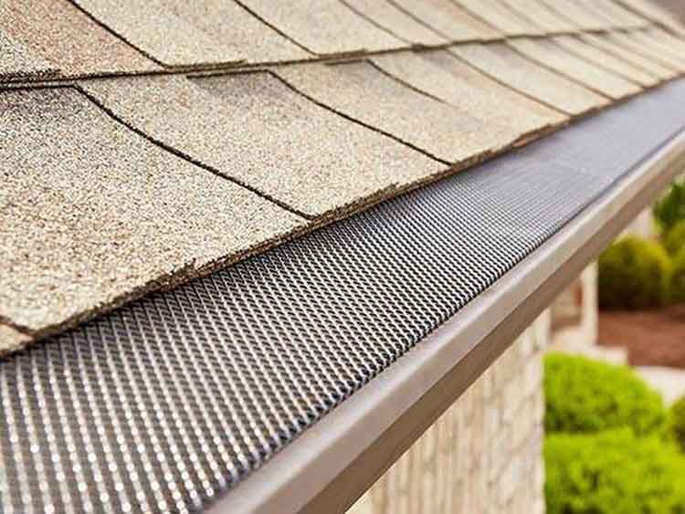 Gutter with mesh cover installed on a roof with brown shingles.