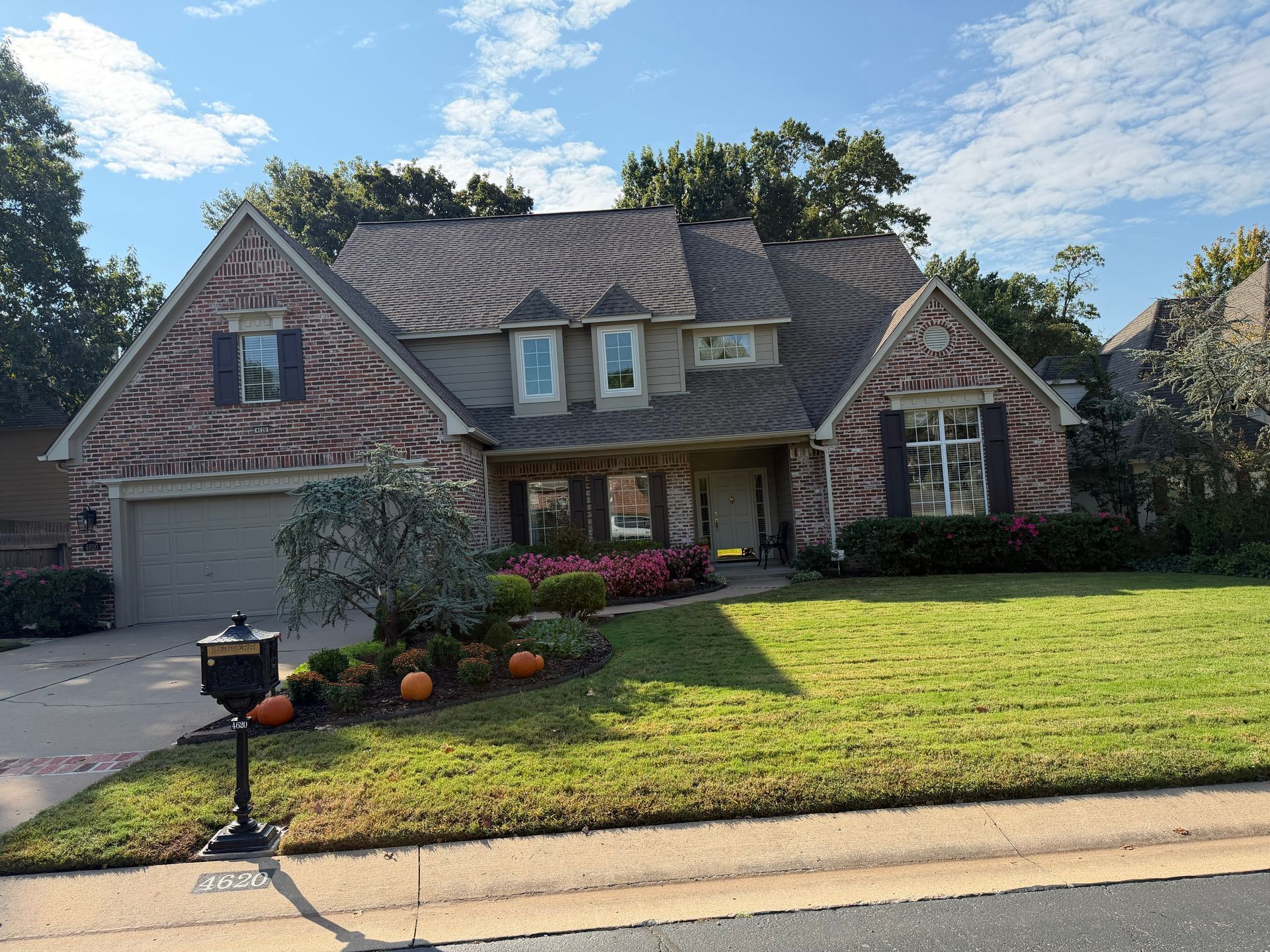 Brick house with green lawn, flowerbeds, pumpkins, and a blue sky.