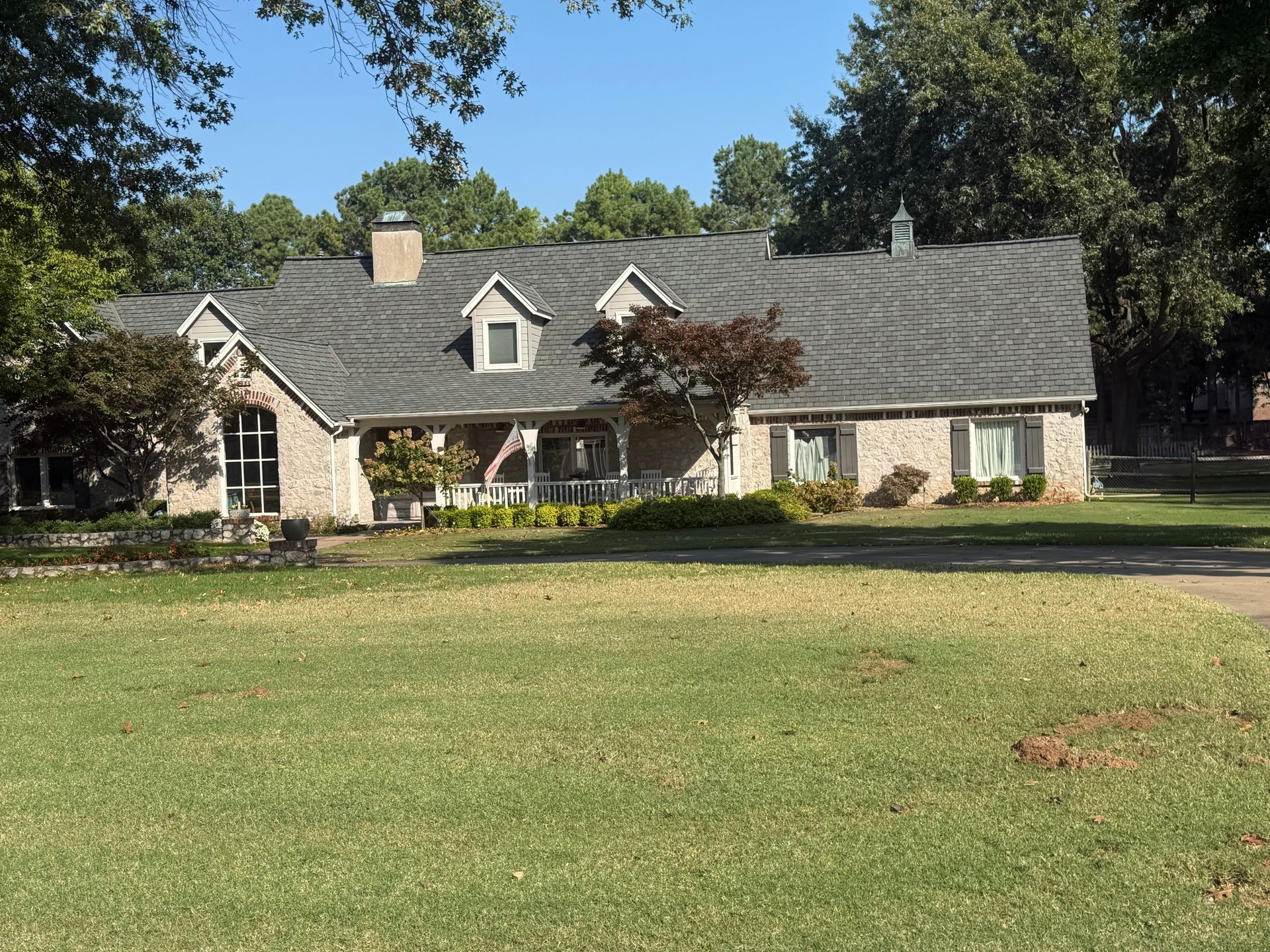 House with gray roof, brick exterior, and green lawn on a sunny day.