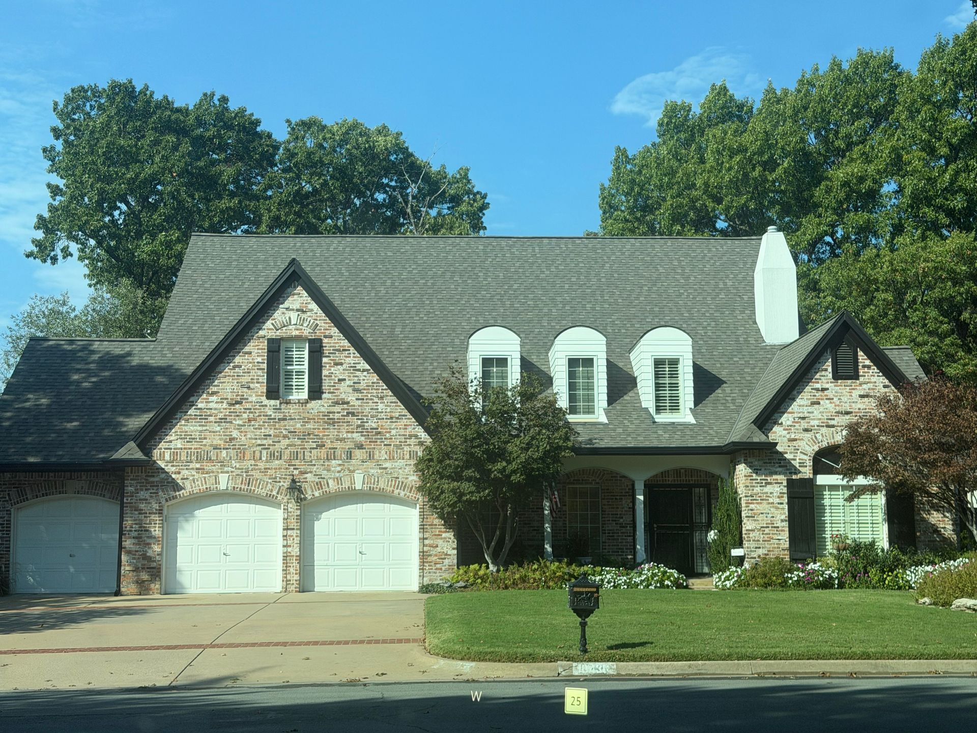 Brick house with gray roof, white garage doors, and front lawn.