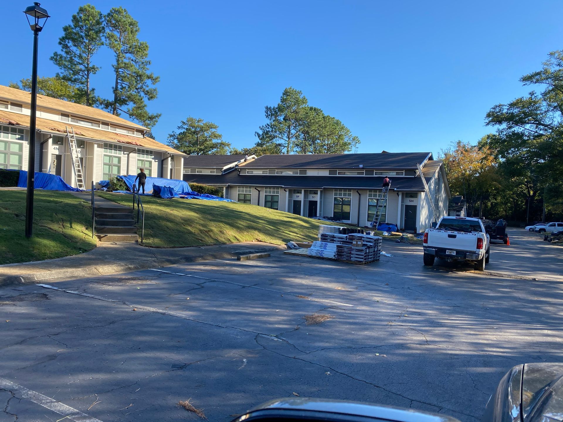 Building under construction with blue tarps, debris, and parked trucks on a clear day.