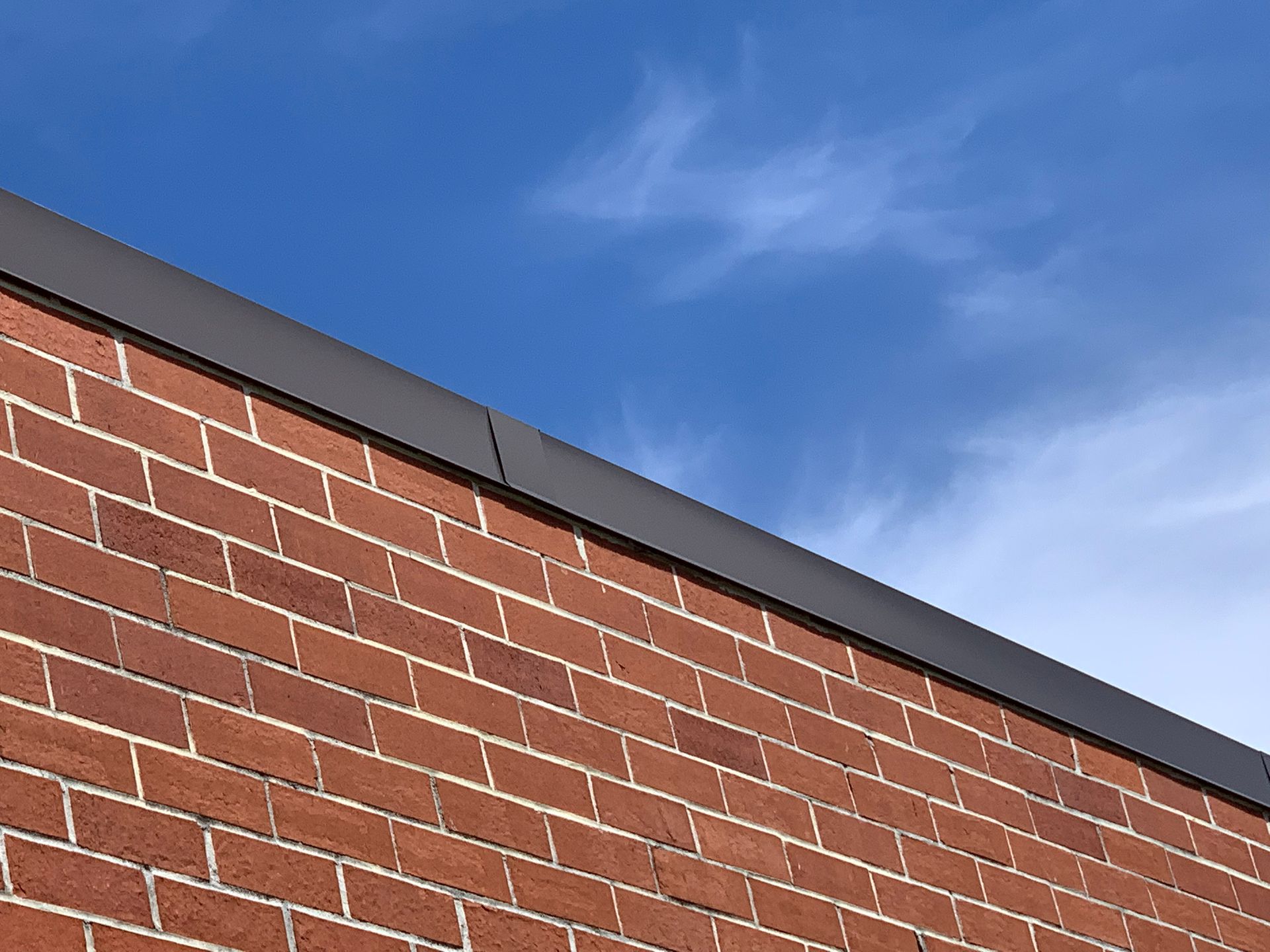 Red brick wall with dark trim against a blue sky with wispy clouds.