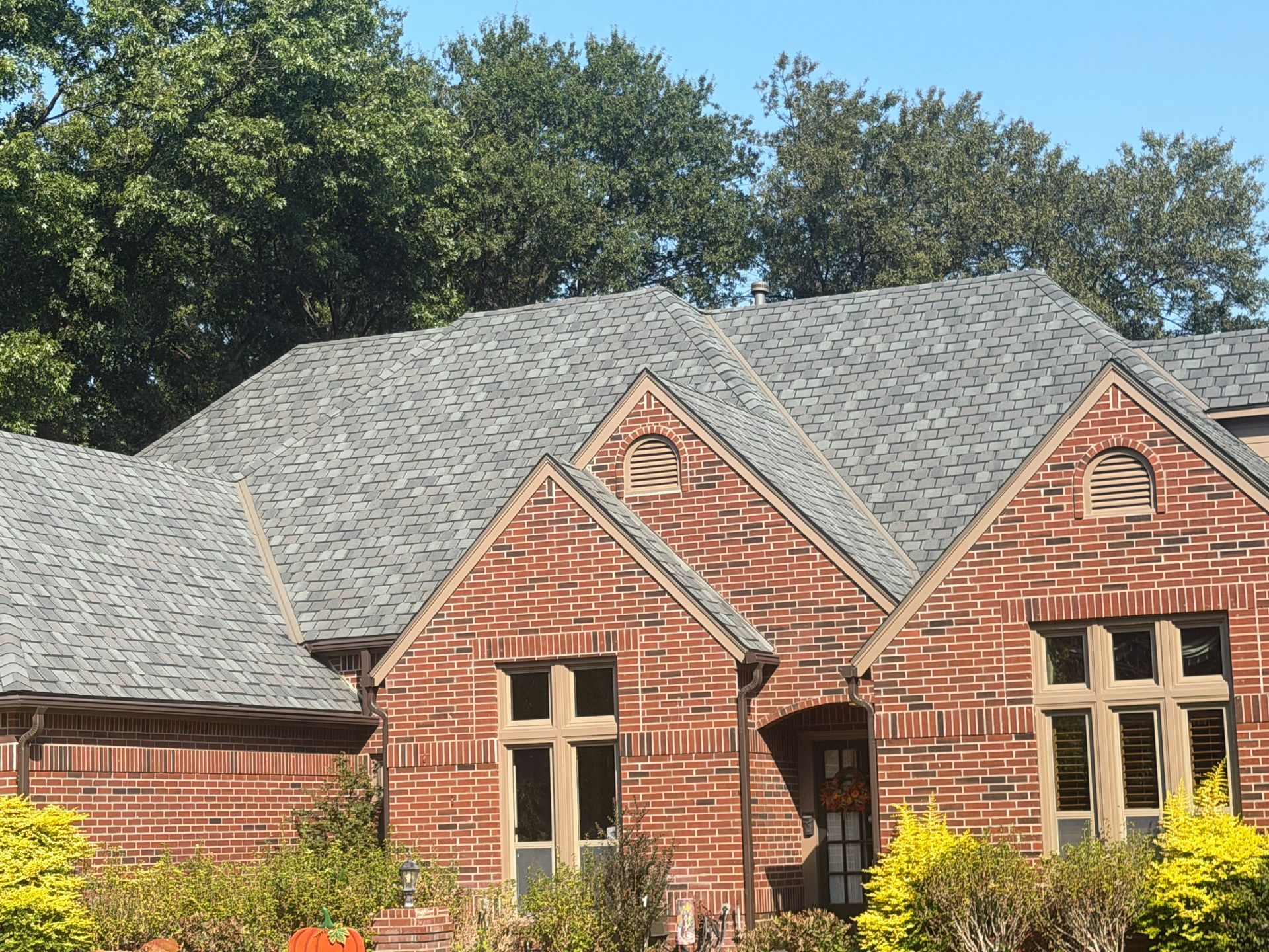Red brick house with grey shingled roof, arched windows, and a clear blue sky.