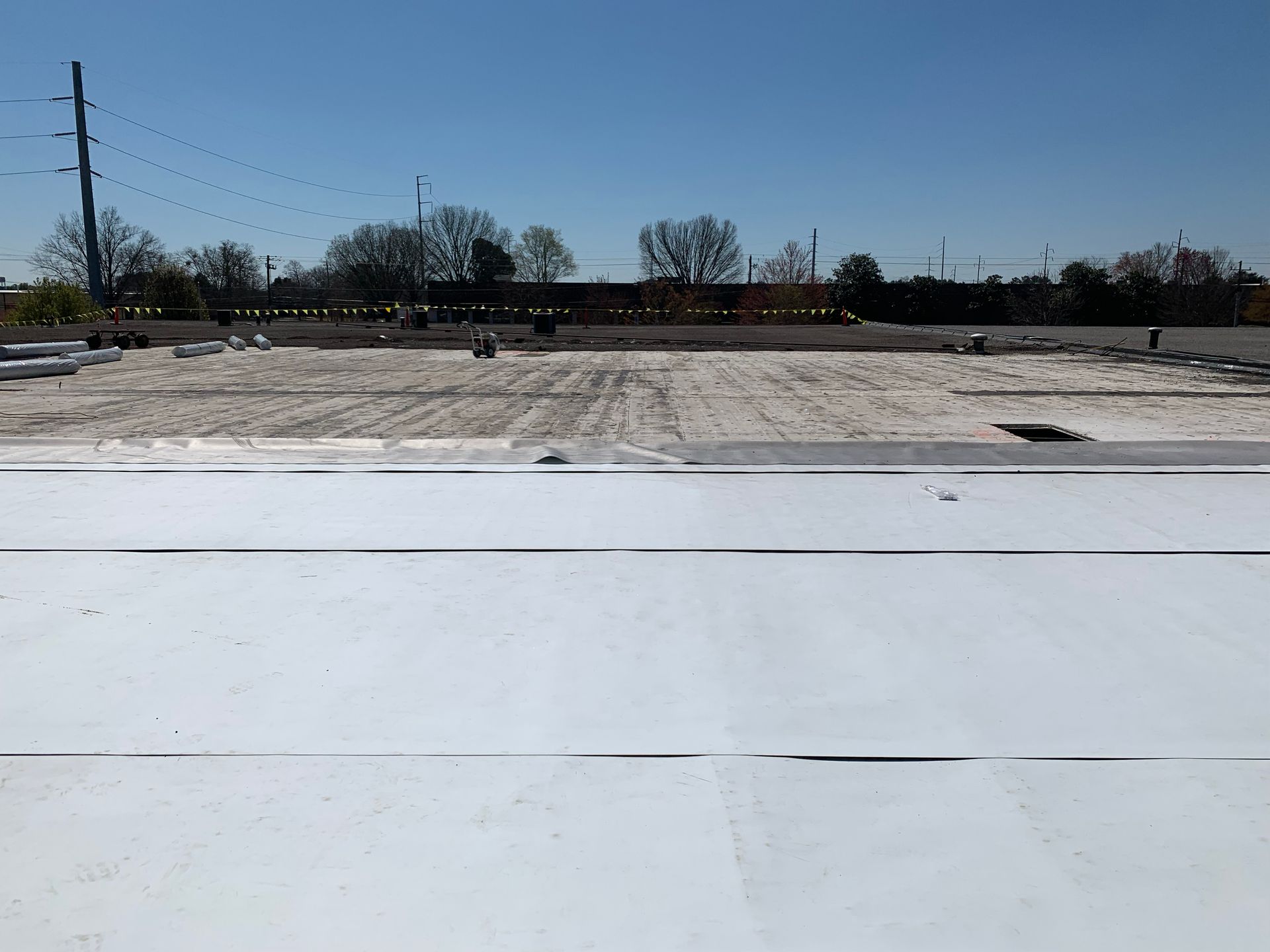 Flat white roof surface with a distant construction site under a clear blue sky.