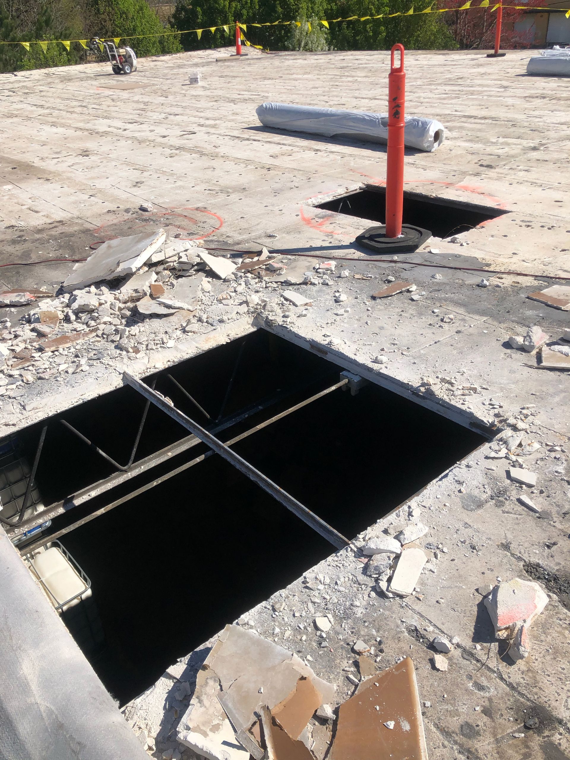 Construction site with open holes in a concrete surface. A warning post stands near one hole. Debris is scattered around.