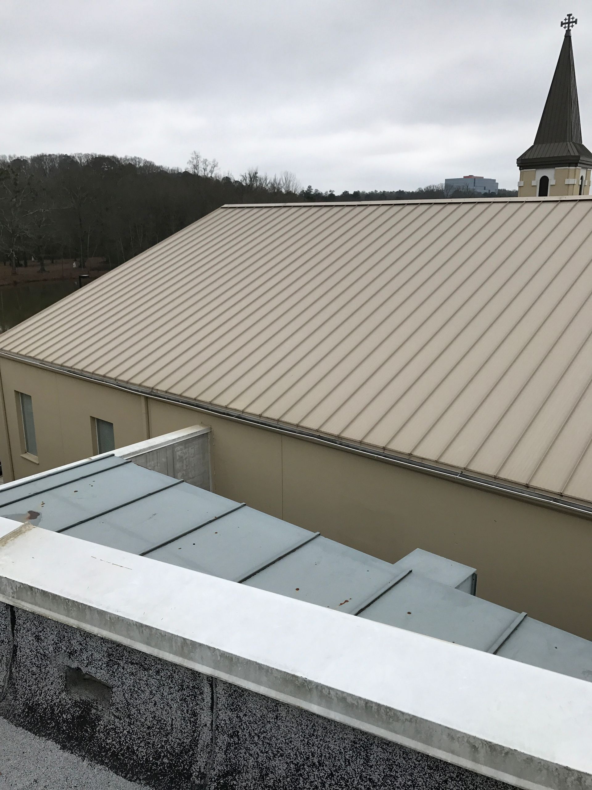 Building with beige metal roof and steeple under overcast sky.