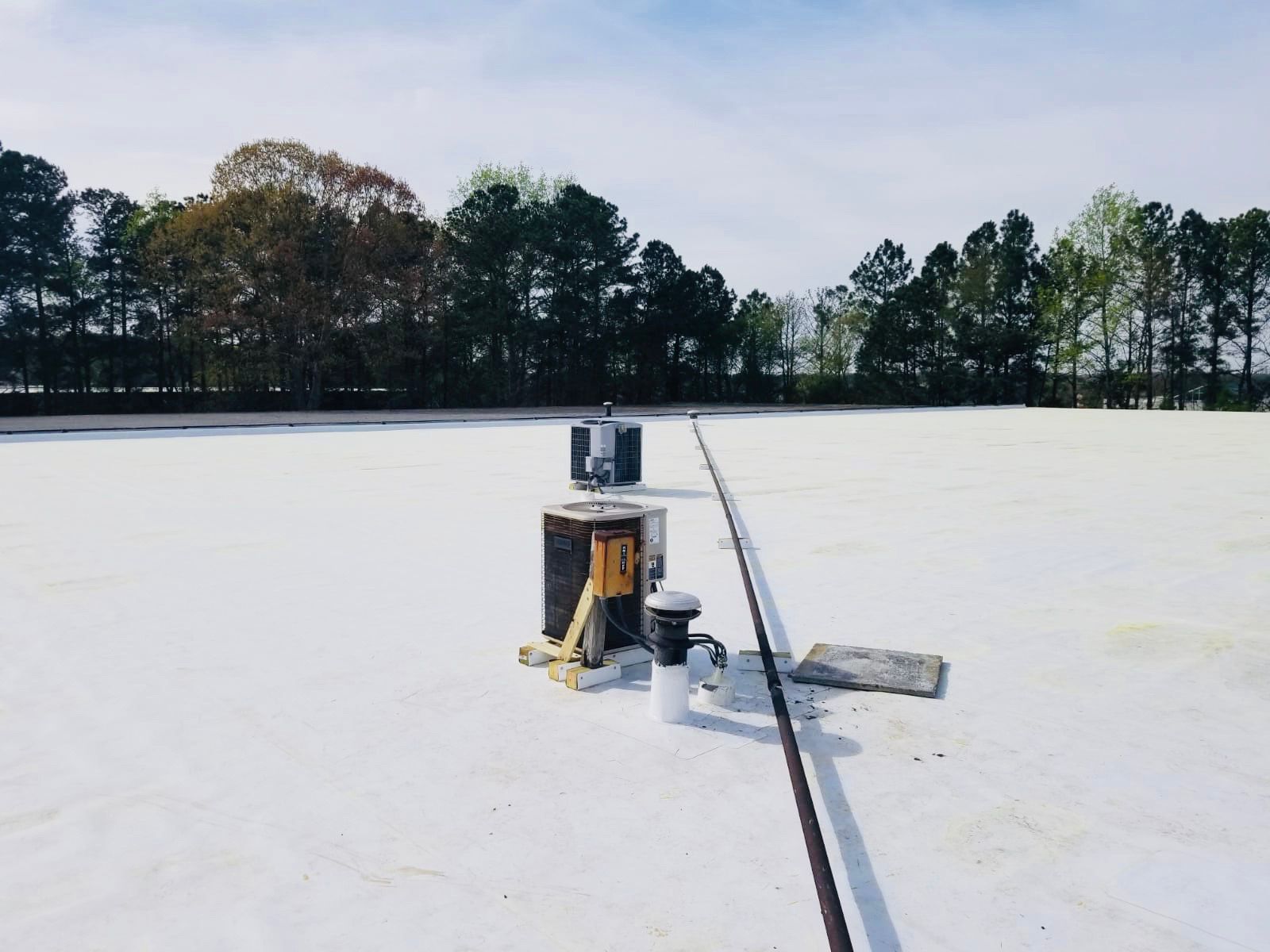 White roof with equipment, trees in background, sunny day.