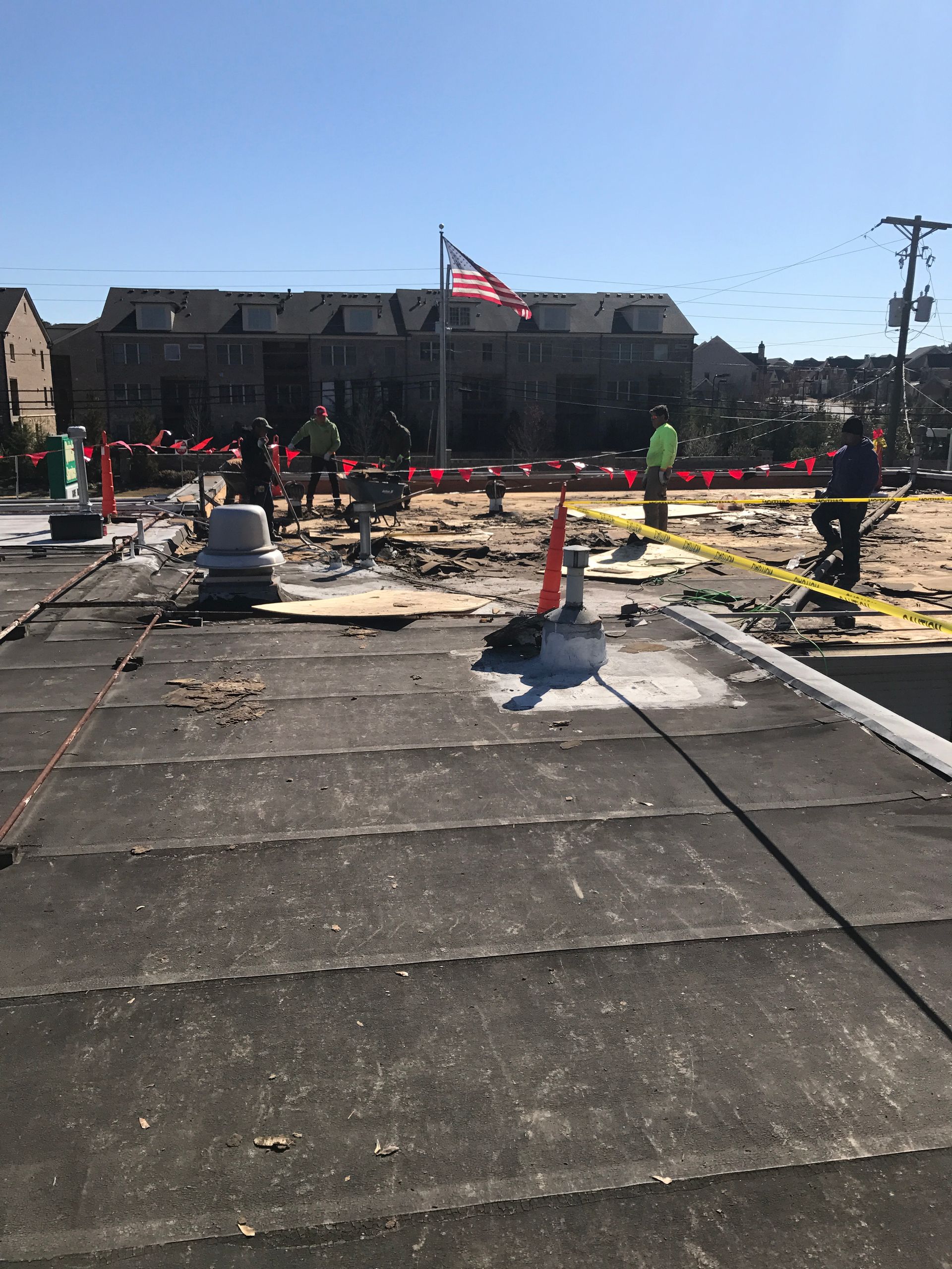 Construction workers on a roof, surrounded by safety cones and caution tape. American flag flies.