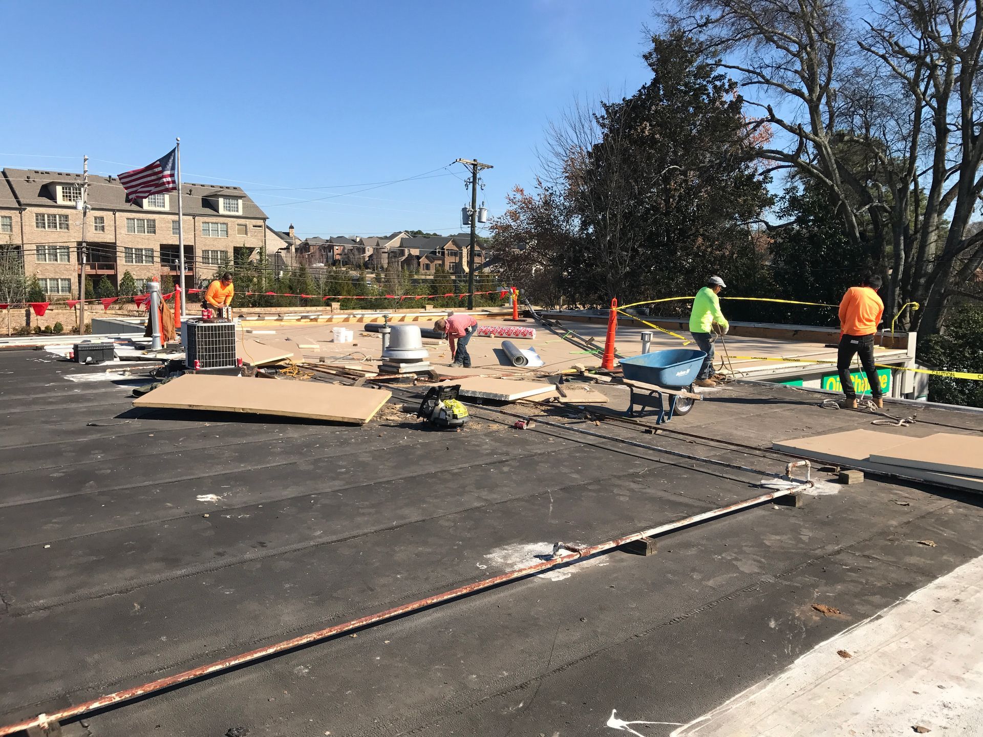 Construction workers on a roof surrounded by safety barriers; a U.S. flag flies in the background.