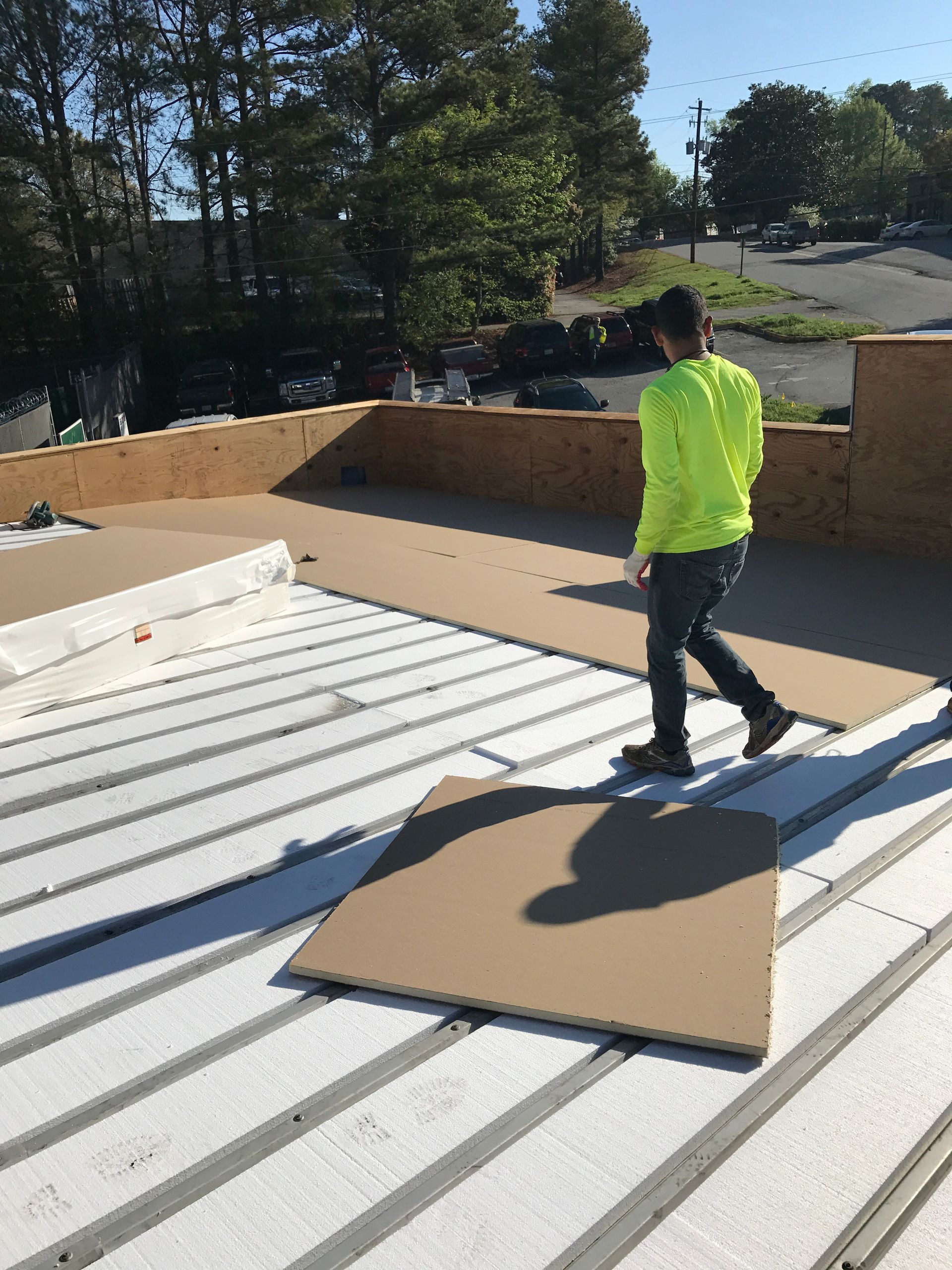 Man in neon shirt walks on rooftop, installing brown boards over white insulation.