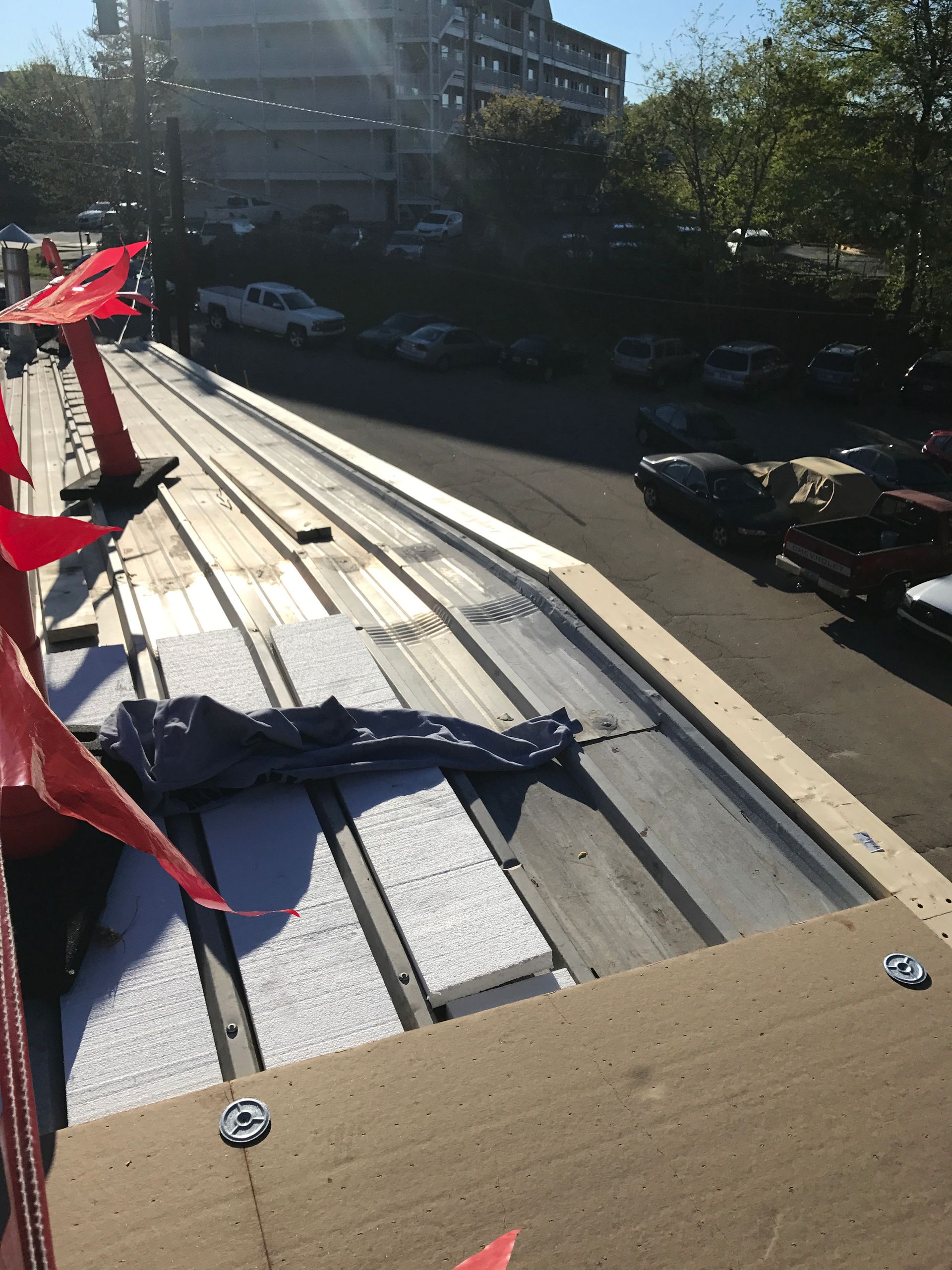 Rooftop construction: Metal panels, insulation, and wooden structure with a street and parked cars in the background.