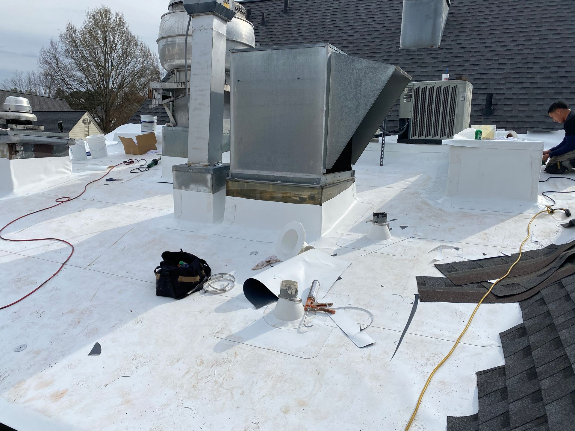 Rooftop with HVAC equipment, white membrane, a worker, and tools.