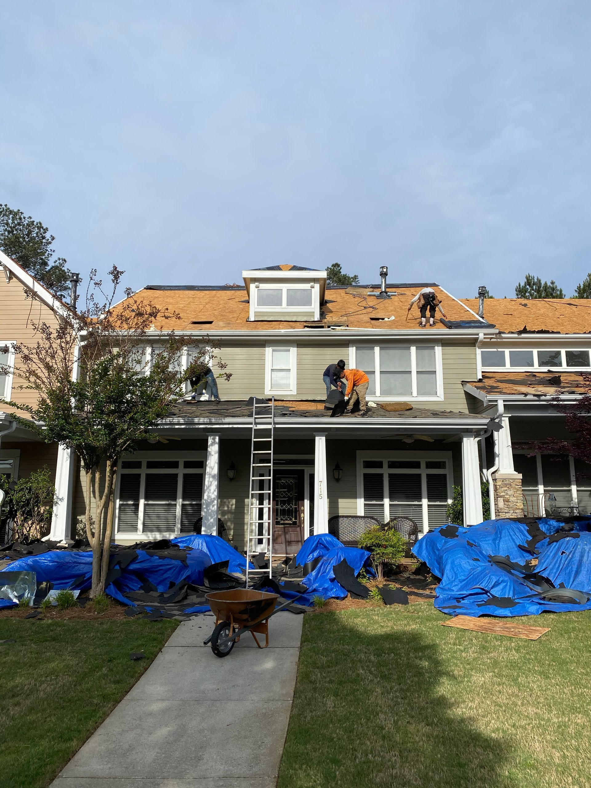 Roofers working on a house with blue tarps on the lawn.