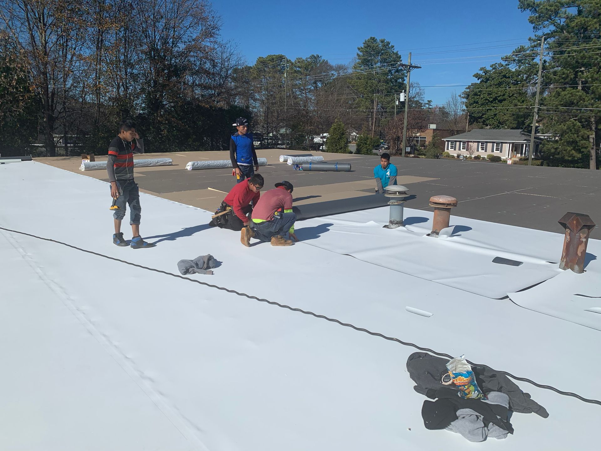 Workers installing a white roof on a building on a sunny day.