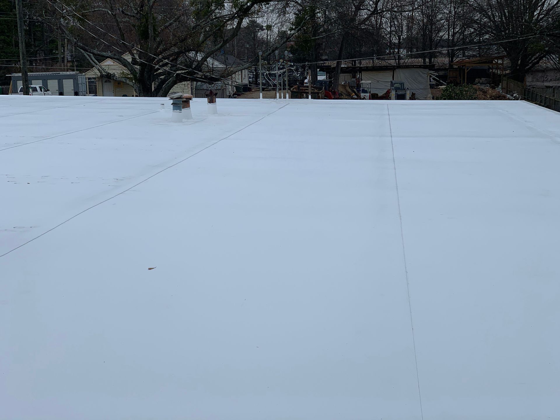Snow-covered outdoor area with two people walking in the distance, near trees and buildings.