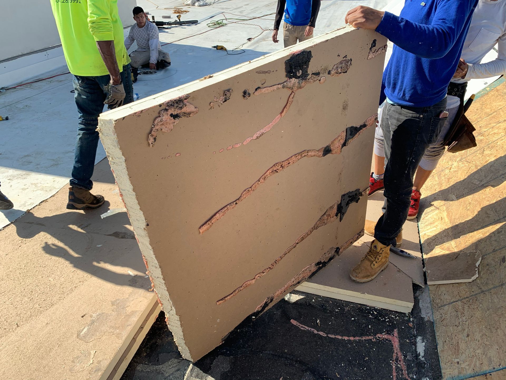 Men on a roof hold a large tan insulation panel with copper wiring.