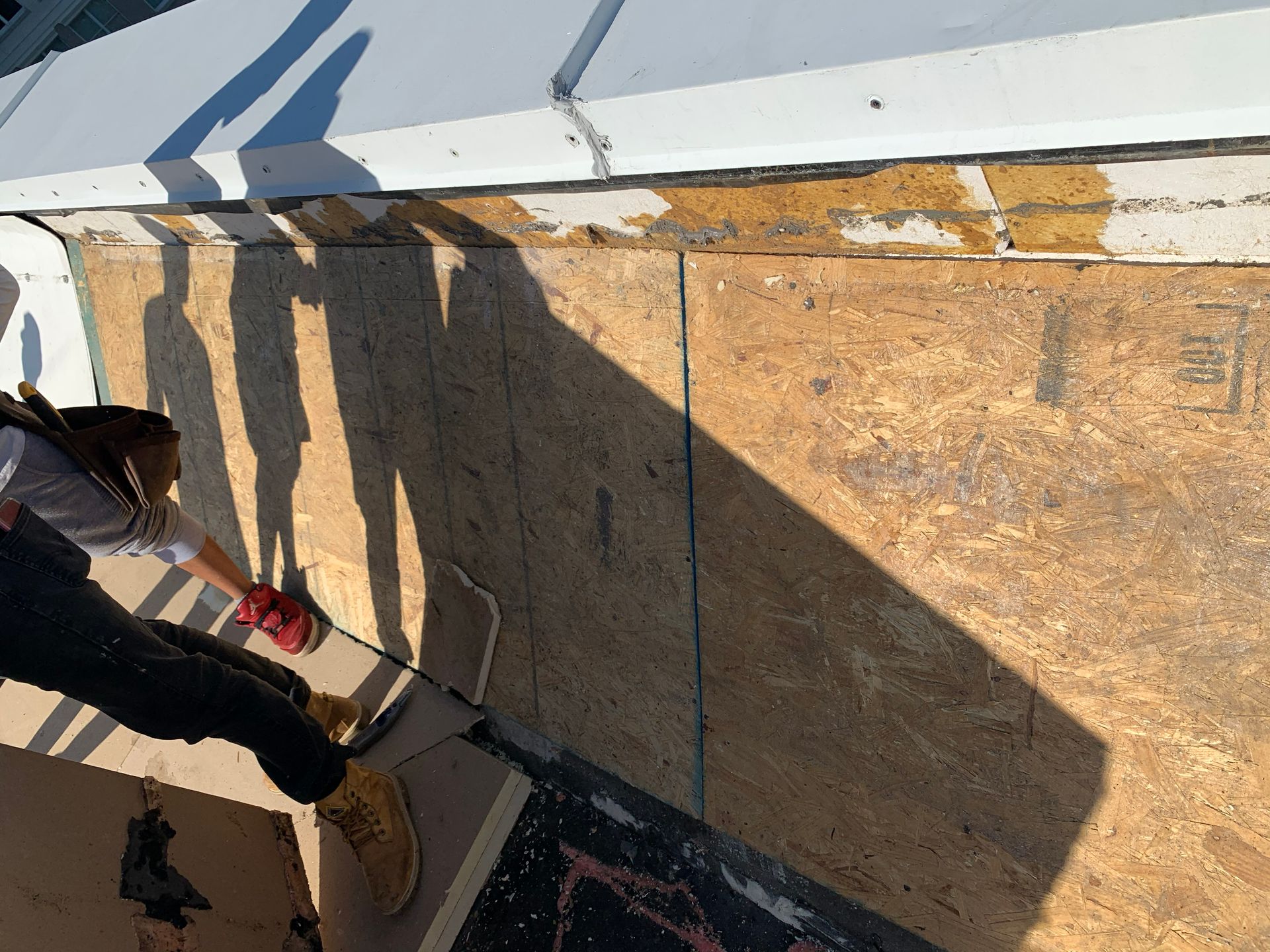 Person on rooftop, inspecting wooden surface. Sunlight casts long shadows.